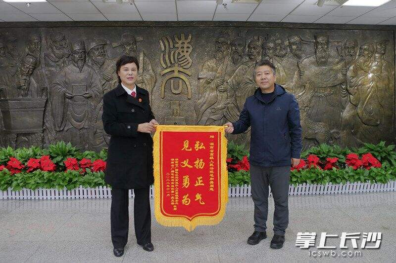 受获救老人所托，湖南省广播电视局工作人员将一面写有“弘扬正气 见义勇为”的锦旗送到毛和英（左）手中。长沙晚报通讯员 李果 摄