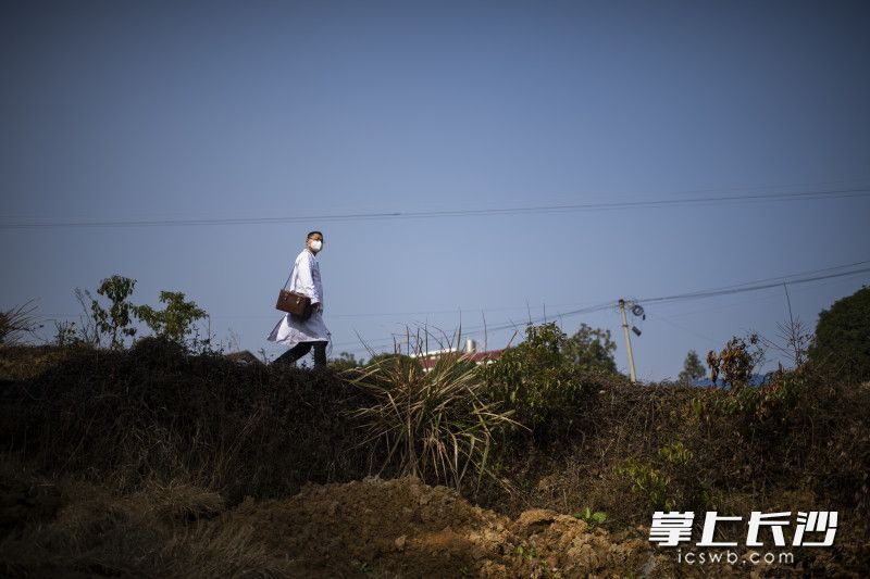 1月12日11时27分，在宁乡市坝塘镇乐安村，乡村医生张杰兵背着出诊箱、手提参数监测仪，穿过村道给84岁孤寡老人送医上门。