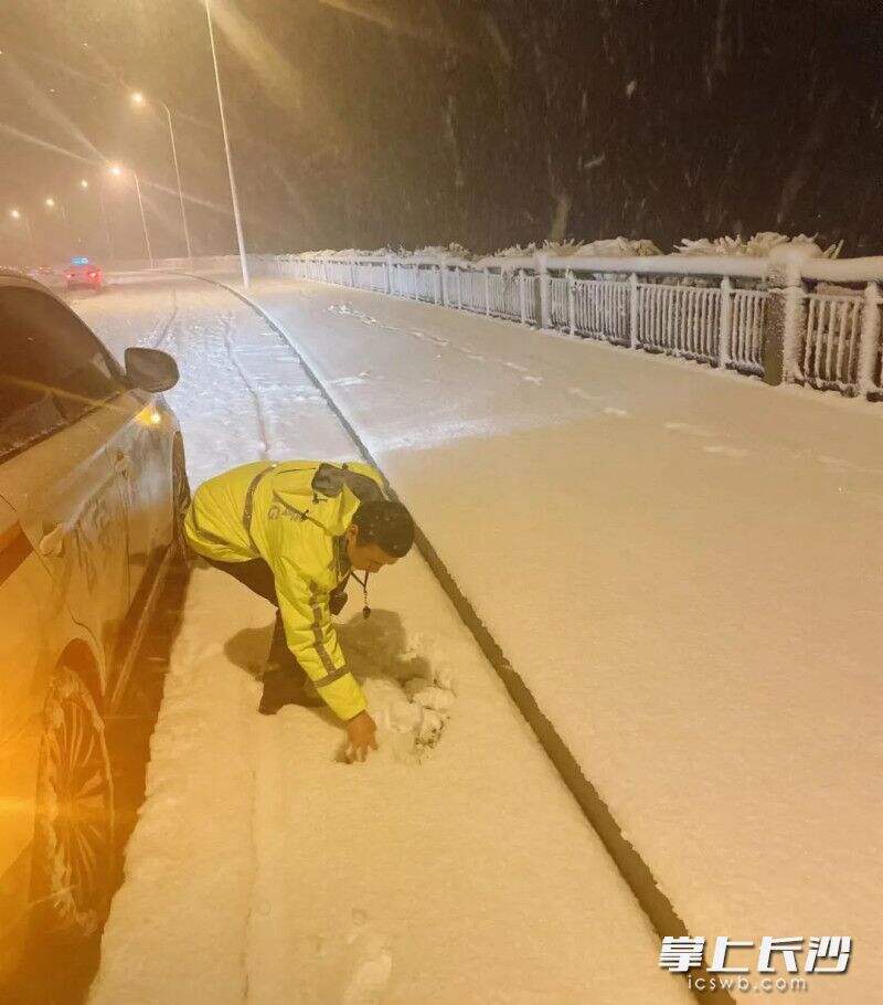 早上6时20分，岳麓交警三中队民警在施家港桥对易结冰路段进行巡查，用手扒开积雪查看路面是否结冰。