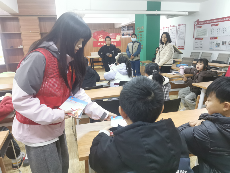 大学生志愿者身穿红色小马甲向听课的小朋友们发放宣传资料。