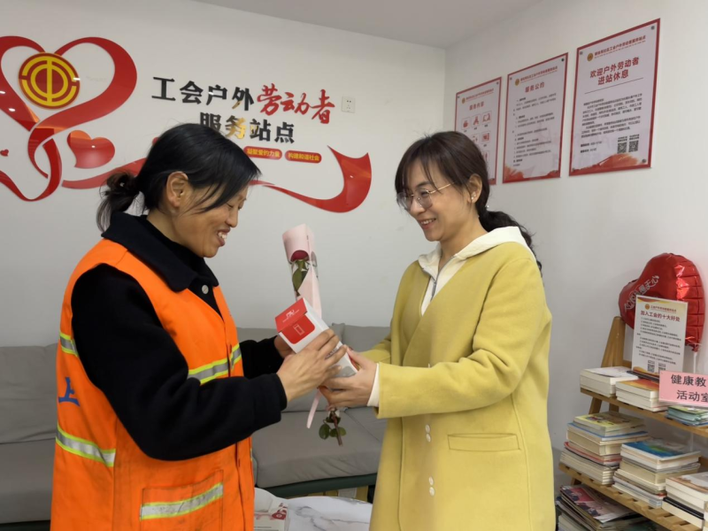 社区工会志愿者将鲜花送给坚守岗位的女环卫工。